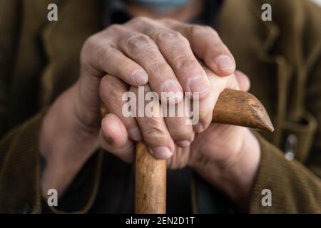 Primo piano sulle mani di un vecchio pensionato caucasico sconosciuto bastone da passeggio per cani da uomo in piedi durante la seduta e l'attesa - persone reali anziano senility co Foto Stock