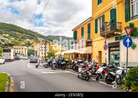 Un gran numero di scooter, motociclette e biciclette a motore park al di fuori di una zona bar con patio in Ventimiglia, Italia, sulla Riviera Italiana Foto Stock