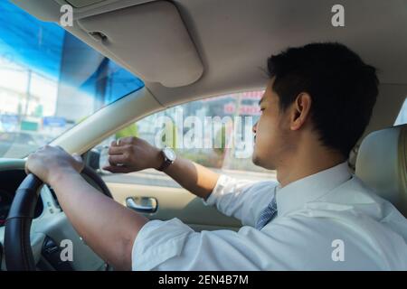 L'uomo asiatico guarda il suo orologio mentre guida per lavorare la mattina, tardi per lavoro. Congestione del traffico Foto Stock