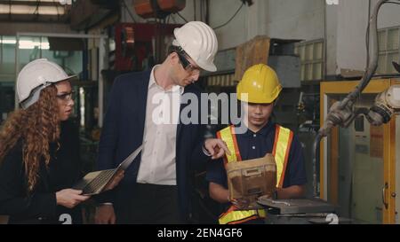 Tre heavy industry business engineering in hardhats discutere di informazioni su computer portatile mentre si è in piedi in interni di saldatura industriale f Foto Stock