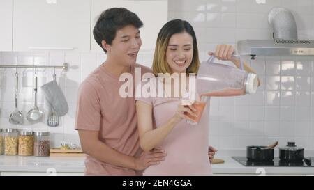 Felice Asiatico bella giovane coppia di famiglia marito e moglie godendo di bere fresco succo di frullato di mela in cucina insieme a casa. Donna versato juic Foto Stock