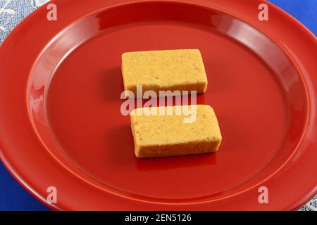 Due pezzi di burro brasiliano di arachidi paçoca caramelle su spuntino rosso piastra Foto Stock