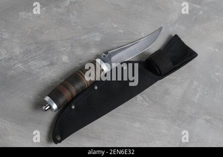 Un elegante coltello da caccia con scabarda e manico in pelle su fondo grigio cemento. Messa a fuoco selettiva. Foto Stock
