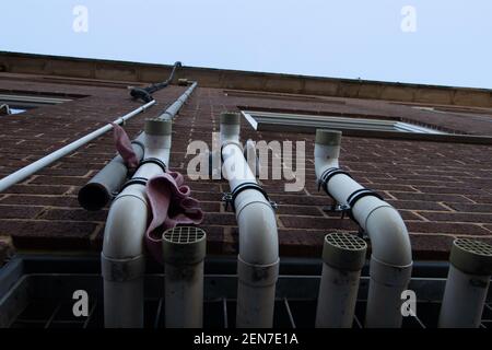 guardando verso l'alto tre tubi in plastica sul lato di un edificio con sfiati e panni scartati Foto Stock