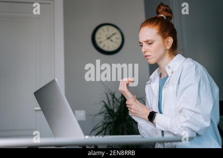 Giovane donna d'affari che soffre di testa rossa che ha dolore al polso durante il lavoro sul computer portatile Foto Stock