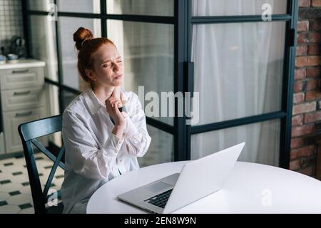 Giovane donna d'affari che ha dolore al polso durante il lavoro sul computer portatile mentre si siede alla scrivania. Foto Stock