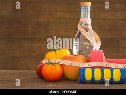 manubri, acqua e metro a nastro su pavimento in legno. Stile di vita e concetto di fitness Foto Stock