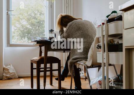 Vista posteriore della donna seduta su una sedia a casa Foto Stock