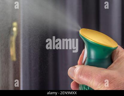 Primo piano POV di un uomo che spruzza mano un deodorante per aerosol da una bomboletta pressurizzata in una stanza interna. Foto Stock