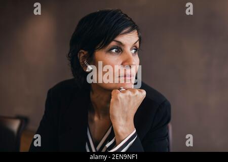 Donna d'affari matura premurosa con la mano sul mento che guarda via ufficio Foto Stock