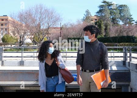 Giovane coppia latina che indossa una maschera protettiva che si guarda l'un l'altro e parla in una stazione ferroviaria. Nuova normalità nel campus universitario. Foto Stock