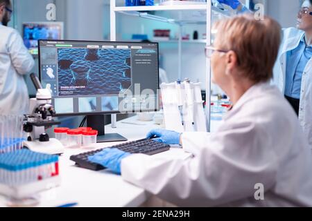 Scienziato medico analizzando un test in computer per la competenza ospedaliera. Medico senior professionista che esamina l'evoluzione del vaccino utilizzando l'alta tecnologia per la ricerca scientifica, sviluppo del trattamento contro il covid19 Foto Stock