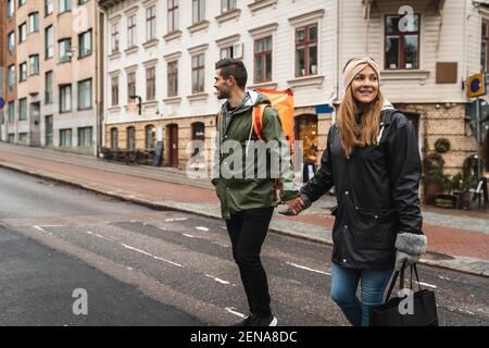 Una coppia sorridente che tiene le mani mentre attraversa la strada in città Foto Stock