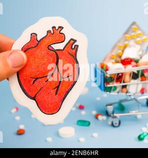 Trattamento o prevenzione di malattie cardiache con varietà di pillole. Matita disegno di cuore umano primo piano in dita sullo sfondo di molti pi colorati Foto Stock