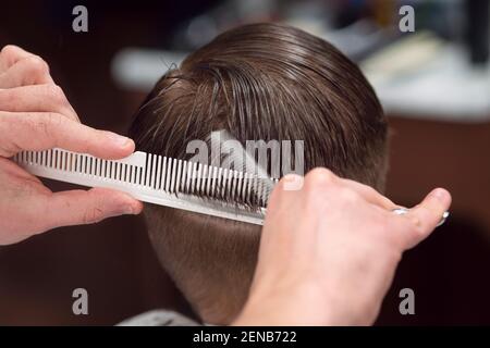 Primo piano di una mano maschile sta tagliando il ragazzo dei capelli Con forbici Foto Stock