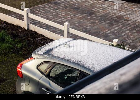 Un ritratto della parte posteriore di un'auto grigia in un vialetto con neve e ghiaccio sul tetto e sulle finestre. Le parti congelate si stanno già sciogliendo. I finestrini dovrebbero Foto Stock