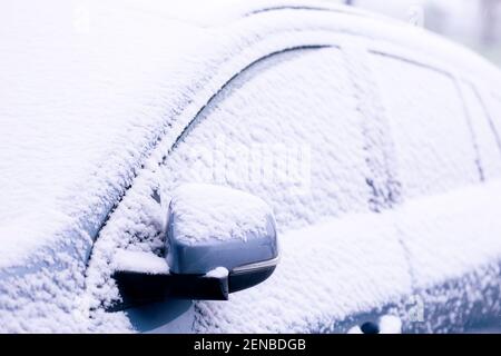 Un ritratto dei finestrini laterali e dello specchio ad ala di un'auto completamente innevata sotto durante una tempesta di neve. Il veicolo è completamente bianco e sh Foto Stock