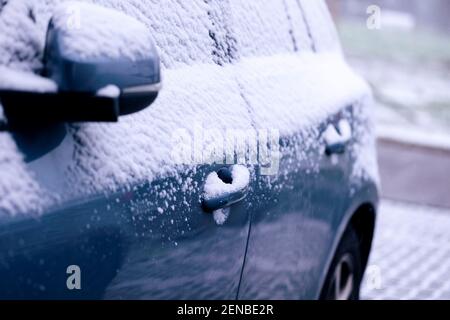 Un ritratto delle porte laterali e dello specchio ad ala di un'auto completamente innevata sotto durante una tempesta di neve. Il veicolo è completamente bianco e shou Foto Stock