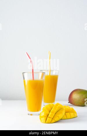 Succo di mango in bicchieri con succo e una paglia su sfondo bianco, mango tritato e intera, deliziosa e sana bevanda dolce naturale Foto Stock