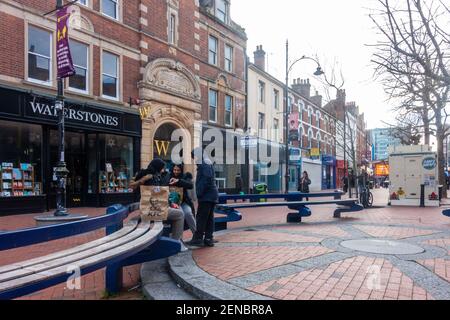 Tre ragazze siedono su una panchina insieme in quella che è una altrimenti tranquilla Broad Street nel centro di Reading nel Berkshire UK. I negozi sono chiusi a causa del COVID-19 Foto Stock