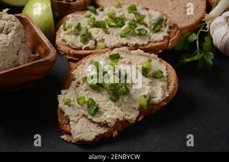 Tradizionale spuntino ebraico vorschmack o forshmak con pane e cipolla verde, fatto di filetto di aringa e servito con pane di segale, fondo di pietra scuro Foto Stock