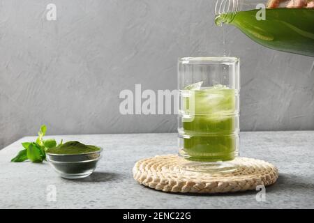 Fare una bevanda di clorella con il cubetto di ghiaccio. Versare la bevanda Detox Chlorella in vetro su un tavolo grigio. Foto Stock