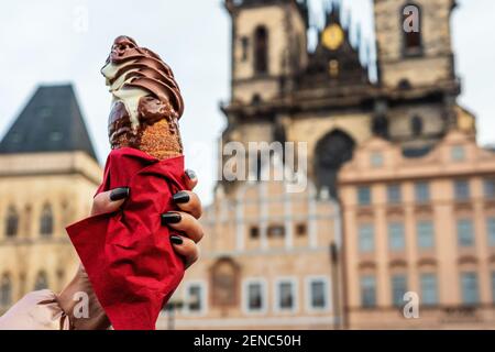 La mano femminile sta tenendo il tradizionale biscotto ceco trdelnik sullo sfondo della città vecchia a Praga. Foto Stock