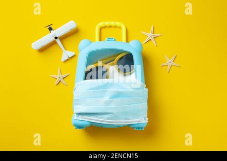 Concetto di viaggio con borsa con maschera medica su sfondo giallo Foto Stock