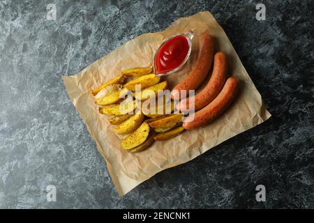 Carta con patata fritta, salsa e salsicce su fondo nero fumé Foto Stock