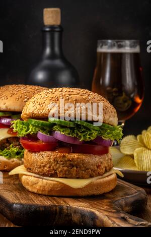 Due gustosi hamburger freschi con bicchiere di birra su un tavolo rustico in legno. Cibo sfondo. Foto Stock