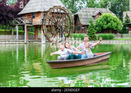 Sorridendo i membri della famiglia in una piccola barca di fronte un mulino ad acqua Foto Stock