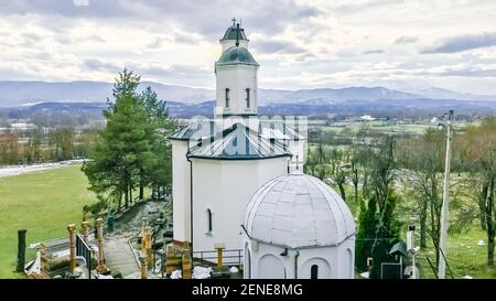 Paesaggio della chiesa ortodossa in inverno con montagne coperte di neve nel giorno nuvoloso, vista posteriore, sfondo religioso Foto Stock