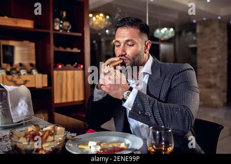 Uomo d'affari che si gode il suo caro sigaro dopo una cena tranquilla Foto Stock