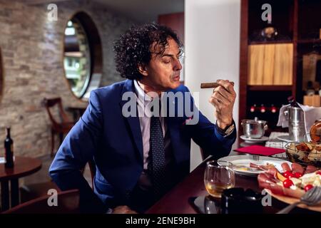 Uomo d'affari che si gode il suo caro sigaro dopo una cena tranquilla Foto Stock