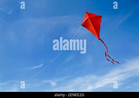 Un aquilone rosso che vola contro un cielo blu. Foto Stock