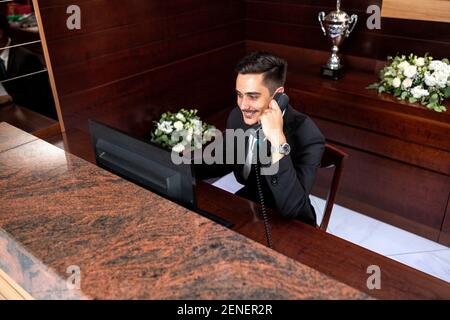 Il receptionist lavora sodo parlando al telefono e gestendo i desideri degli ospiti Foto Stock