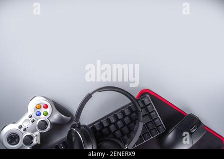 Concetto di dispositivi di gioco e di gioco. Spazio tavolo di lavoro del giocatore sfondo, vista dall'alto. Tastiera, mouse, joystick gamepad, tappetino per mouse e cuffie. Su ta grigio Foto Stock