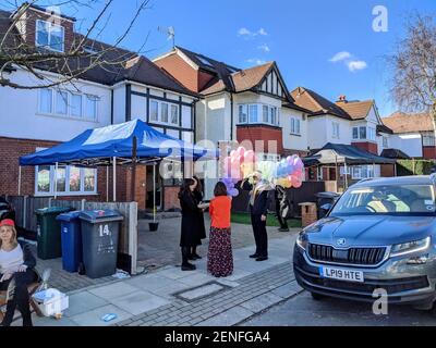 Le celebrazioni per la festa ebraica di Purim (Festival dei lotti) iniziano a Golders Green, North West London, con famiglie e bambini che si godono il cielo blu e il sole mentre si riuniscono in abiti eleganti. Gazebo eretto di fronte alle case in una strada residenziale in una comunità ebraica locale. Londra, Regno Unito. 26 febbraio 2021. Foto Stock