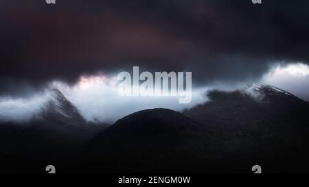 Condizioni atmosferiche estreme nelle Highlands Scozzesi all'alba. Nuvole scure sui picchi di montagna e inversione di nuvole nella valle. Foto Stock