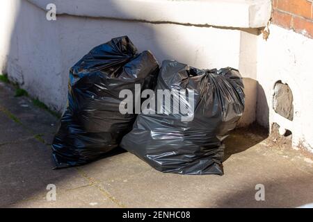 Due sacchetti di rifiuti neri pieni o sacchetti di contenitori neri all'esterno una casa pronta per la raccolta di bidone Foto Stock