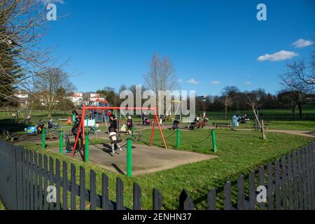 La gente gode del sole e del cielo blu nel Sunny Hill Park, a nord-ovest di Londra, i bambini e le famiglie nel parco giochi. Inizio di un weekend soleggiato con cielo blu. Regno Unito Meteo. Londra, Regno Unito. 26 febbraio 2021. Foto Stock