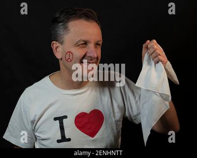 Un uomo con il simbolo della pace e dell'amore dipinto sul suo viso tiene un fazzoletto bianco e indossa un t-shirt che dice che amo Foto Stock