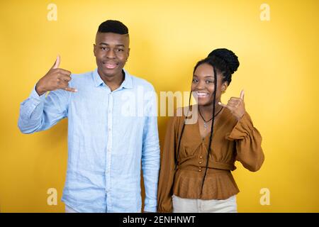 Giovane coppia afroamericana che si erge su sfondo giallo gridando con espressione pazzesca facendo rock simbolo con le mani in su Foto Stock