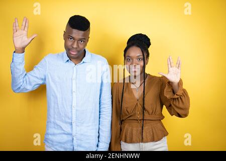 Giovane coppia afroamericana in piedi su sfondo giallo facendo stella simbolo trek freak Foto Stock
