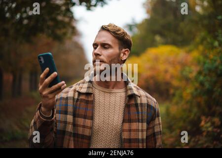 Bell'uomo che usa il telefono cellulare mentre passeggi in autunno foresta Foto Stock