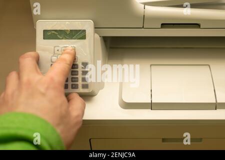 la mano di una persona o di un addetto all'ufficio preme i pulsanti sul pannello di controllo di una stampante, di una copiatrice o di una periferica multifunzione Foto Stock