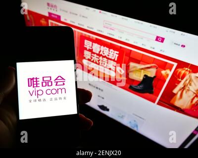 Persona titolare smartphone con logo della società cinese Vipshop Holdings Ltd (VIP.com) sullo schermo di fronte al sito web. Mettere a fuoco il display del telefono. Foto Stock