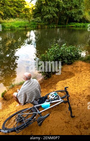 Nuotatore seduto accanto al fiume con la bicicletta Foto Stock