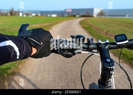 Un manubrio di bicicletta visto dalla prospettiva della prima persona e con una mano mans sul manico. Computer da bici e campana visibili. Foto Stock