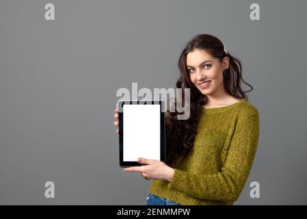 giovane donna emozionale che mostra un tablet con schermo touch vuoto con spazio di copia, isolato su sfondo grigio Foto Stock